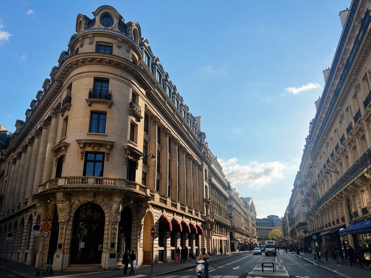 Immeubles haussmanniens à l'angle d'une rue parisienne, sous un ciel bleu de fin de journée